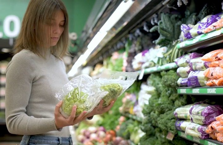 Shopper standing by vegetable chiller section of supermarket comparing two lettuces