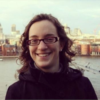 The profile of Dr Laia Becares wearing glasses and a dark coat with the Thames bank in London behind her