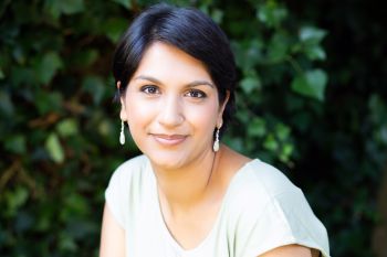 Angela Saini is pictured in a white top smiling gently at the camera outside