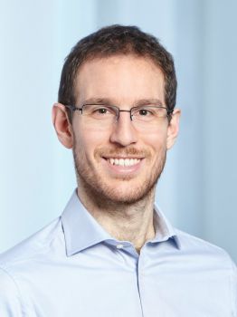 Portrait of Fields Medalist, Prof. Alessio Figalli. A headshot of a man smiling and wearing glasses, wearing a blue shirt