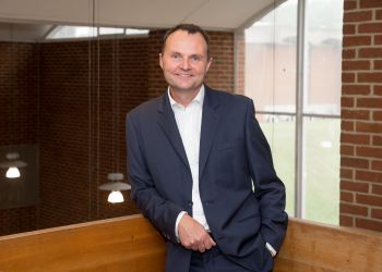 University of Sussex Vice-Chancellor Adam Tickell leans on a stair bannister wearing a dark blue suit and white shirt