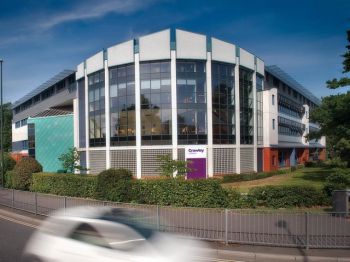 A view across the road of Crawley College - a modern looking glass fronted building set behind a small hedgerow