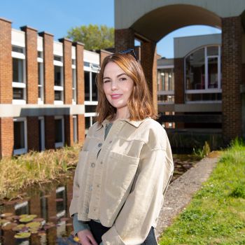 Female standing in front of university building with hands together and smiling