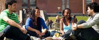 Four students sit cross legged facing each other with the University of Sussex library in the back