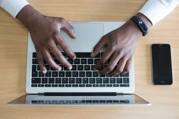 A view from above of a laptop and a mobile phone with two hands reaching out to touch the laptop keyboard