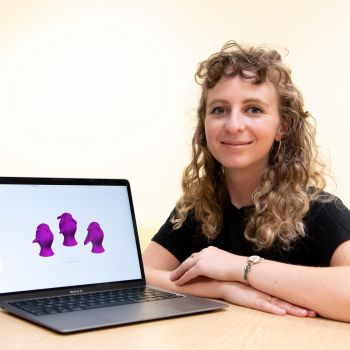 Claire Lancaster is wearing a black top and sits beside a computer screen displaying three purple images on a white background