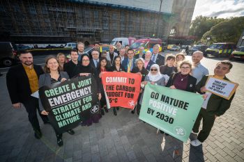 A group of men and women stand together holding signs outside the Houses of Parliament