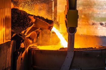 Hot molten metal is poured into a large container at a steel factory