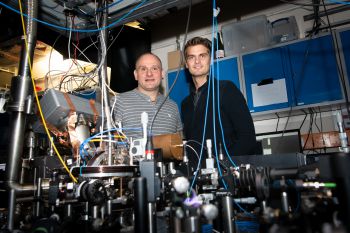 Two men standing behind an intricate display of wires and electronics