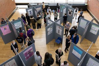 An overhead shot of the JRA posters exhibition showing academic posters on display boards, a crowd milling around them.