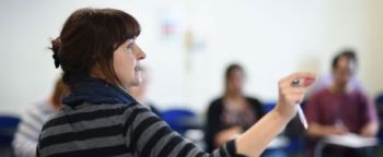 A female researchers teachers a training workshop at the front of a class of students.