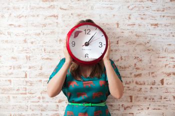 Woman holding a clock up to cover her face.