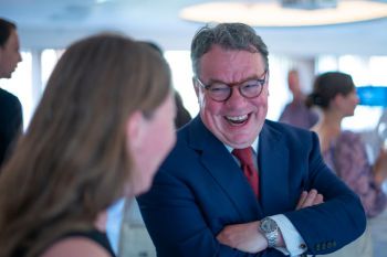 Man smiling with arms folded standing talking to event guests