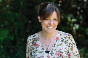 Lucy Owen-Collins wears a flowery top and smiles at the camera in an outdoors setting