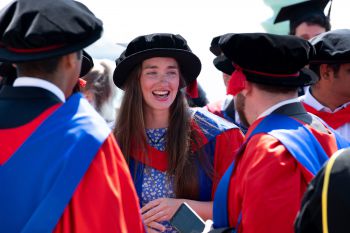 A smiling Rosemary Coogan is dressed in graduation mortar board and gown on a sunny day