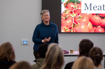 The Vice-chancellor, Sasha Roseneil, stands in front of the audience, speaking and gesturing as she introduces the workshop