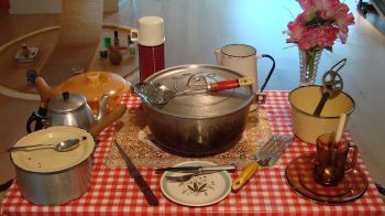 Image of a kitchen table covered with cooking utensils including pots, pans, knives and forks