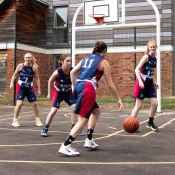 women basketball players in red and blue kits playing on a basketball court