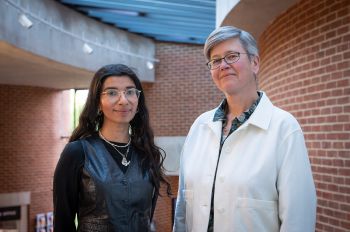 2 people facing forwards, standing side by side smiling, in the ACCA building. On the left Nabihah Iqbal, on the right VC Prof. Sasha Roseneil