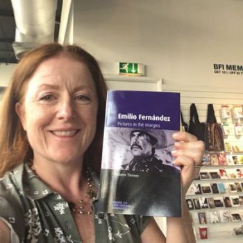 Dolores posing with one of her recently published books. She has red hair and light skin.