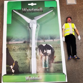 photograph of Micheal dressed in high vis lying down next to a windmill packaged up with batteries
