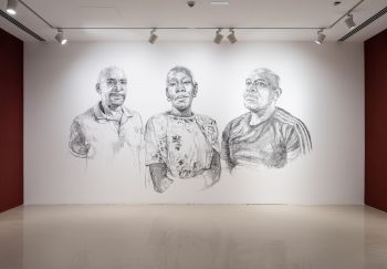 3 large black and white portraits sketched onto a white wall. A black woman centre, 2 black men each side. Her face is conveying a mix of strength and vulnerability, intricate charcoal strokes create a compelling and emotive portrayal of the subject.