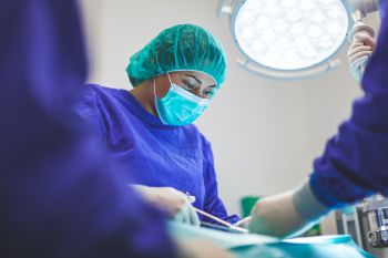 A woman in blue scrubs operating in a surgical theatre