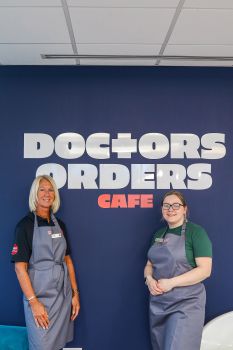 two baristas standing in front of cafe sign