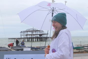 A scientist in a lab coat laughing and holding a Soapbox Science umbrella in front of the West Pier