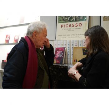 Photograph of two people from behind having a conversation,looking at a book