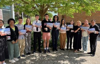 A group stands in the sun outside Essex House holding certificates