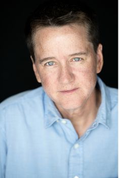 A photo of Heather K. Love who is in front of a black background wearing a blue shirt