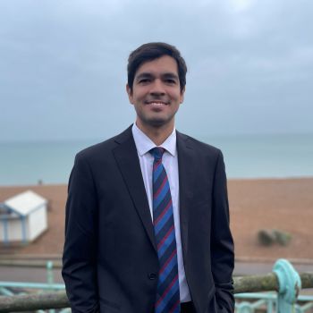 Sebastian Rodrigues, smiling at the camera in a suit with Brighton beach in the background