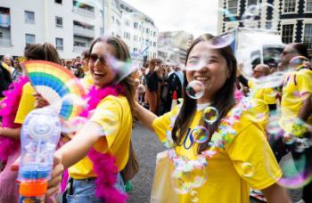 Two women wearing University of Sussex t shirts blow bubbles in the Pride parade