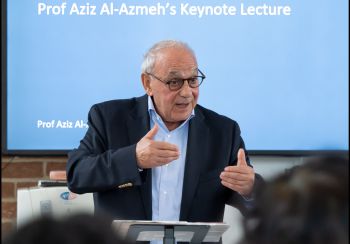 A man with glasses delivering a lecture in front of a screen