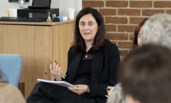 A woman sitting down with a notebook on her lap, talking