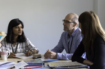 A female trainee social worker talks to two other adults around a table in a Local Authority office