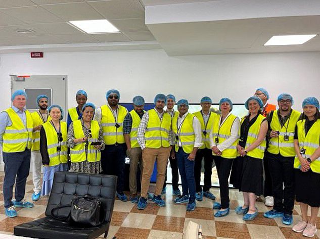 MBA students at the De'Longhi production plant, with Rudi Sperandio, Plant Operations Director and Vasco Buffolo, Plant Quality Manager. All people are wearing high visability jackets and blue hair nets