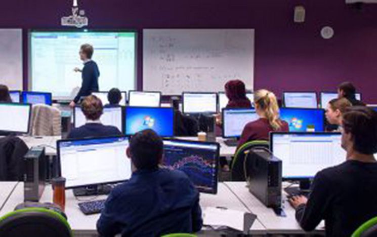 A classroom with PhD students sat at computers looking at a screen being actively taught