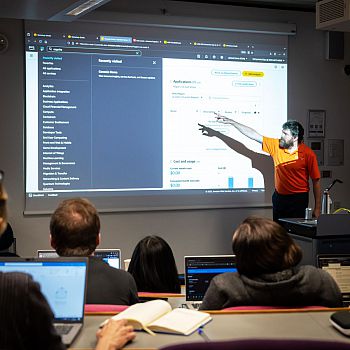 Person presenting to a group of people and pointing to information on a slide.