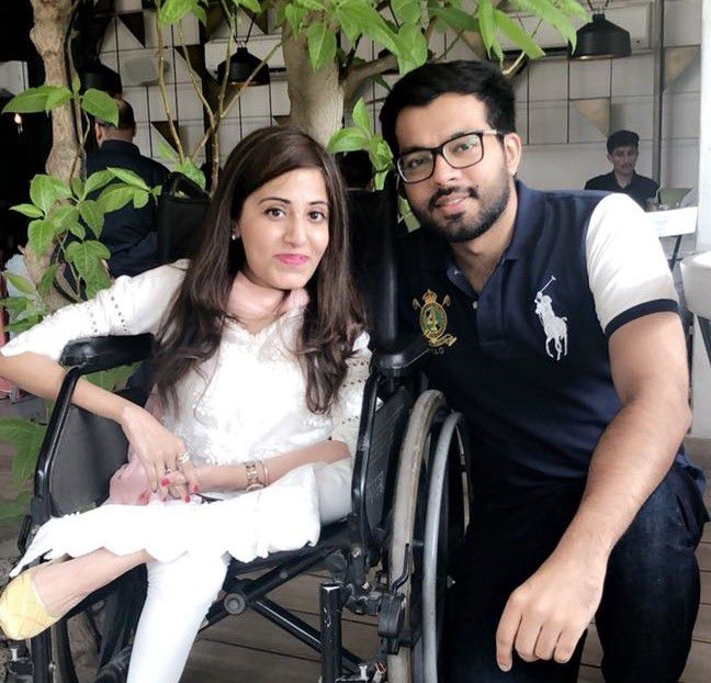 Photo of Muhammad and his friend and partner Amna. Muhammad is kneeling to the right of Amna, who is sitting in her wheelchair. Both are smiling at the camera